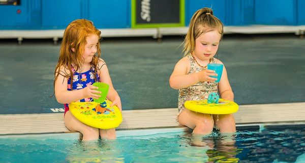 Two girls sitting on the water's edge with flotation boards at Christchurch Recreation and Sport pool. 