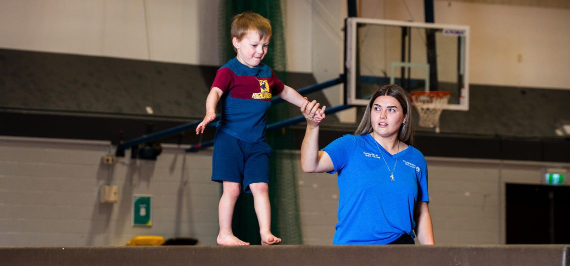 An instructor helping a child walk on a balance beam during a pre-school gymnastics class at Christchurch Recreation and Sport centre. 