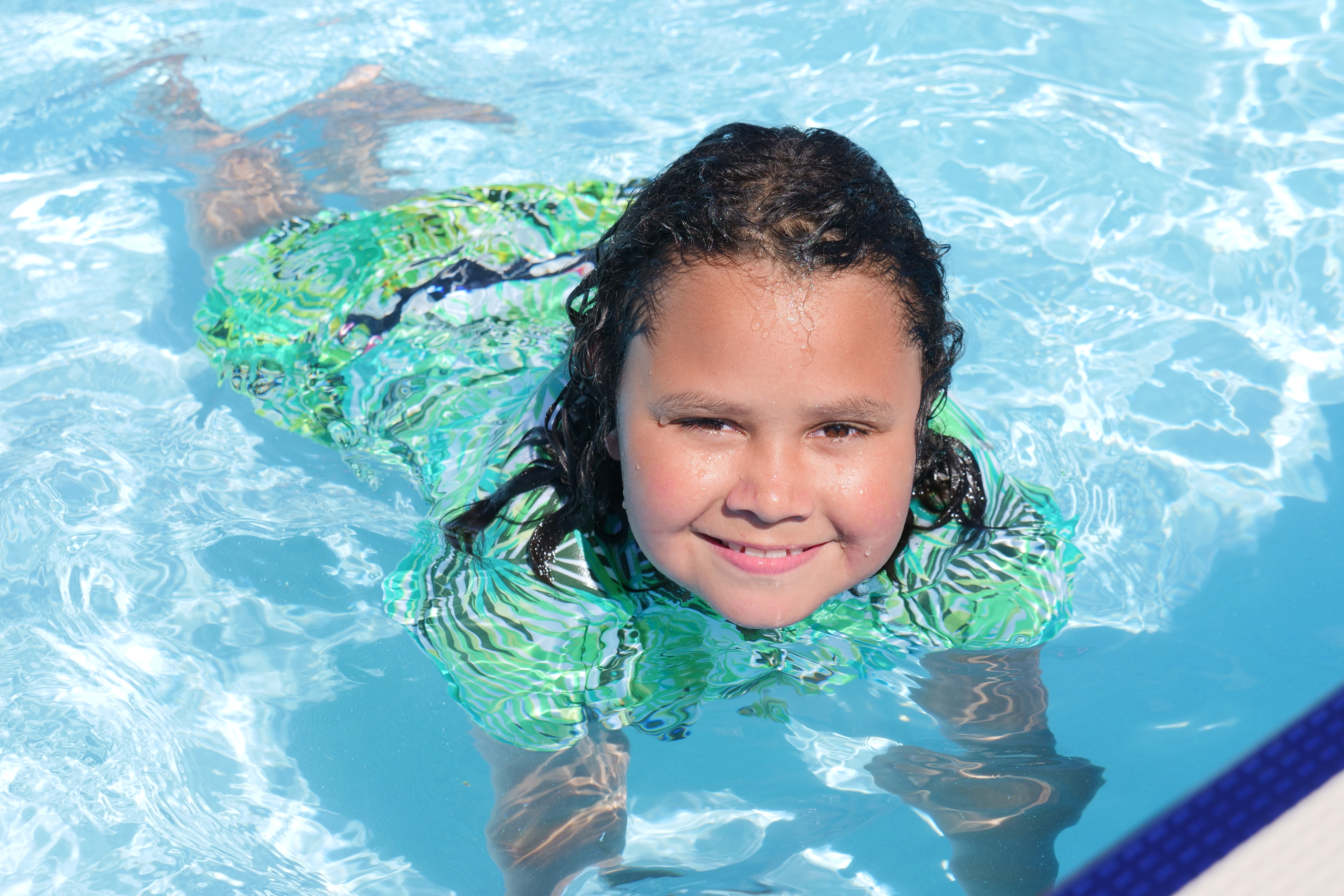 A smiling girl in green swimmers in the toddler pool at Waltham Summer pool. 