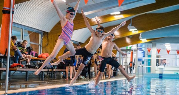 A group of smiling children jumping into the water with arms out at Christchurch Recreation and Sport pool. 