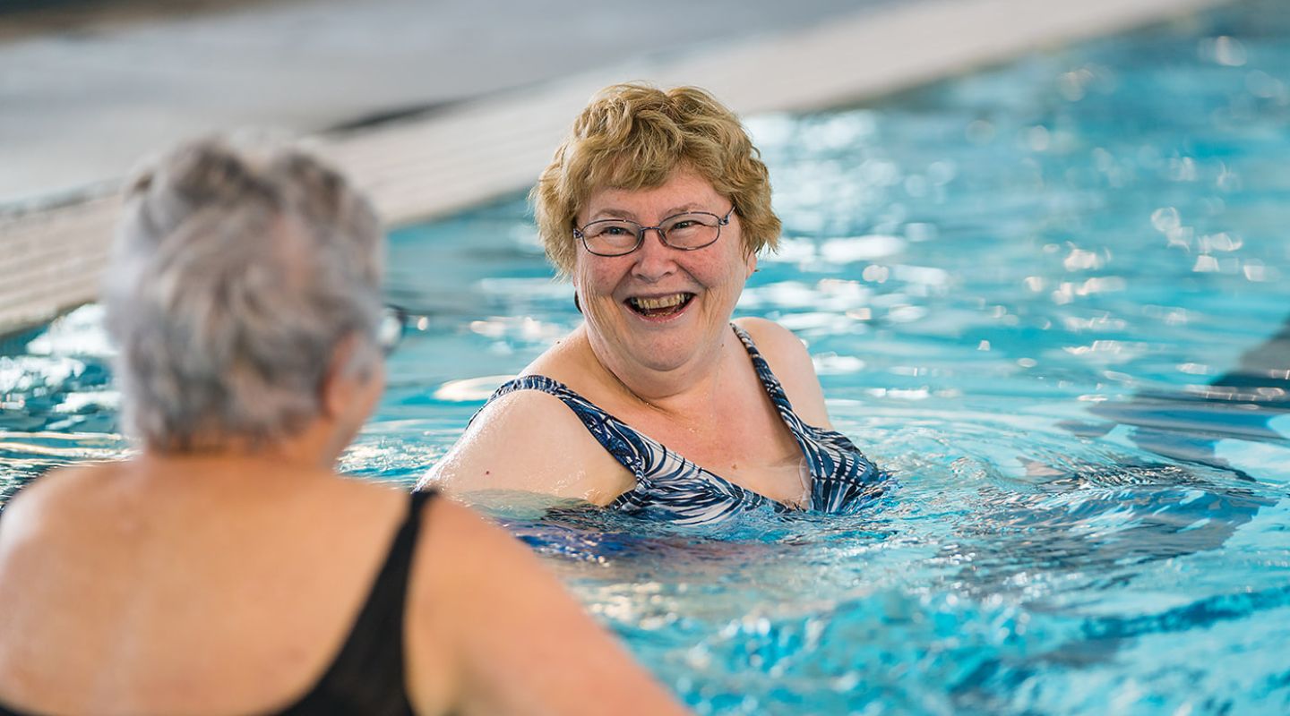 Two older women smiling in the pool while participating in an Aqua gentle class at a Christchurch Recreation and Sport pool.