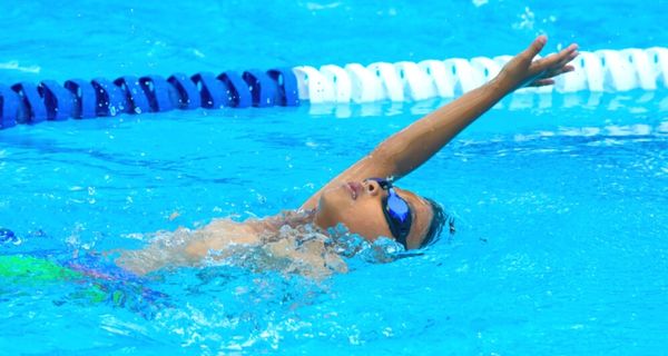 A child in a blue swim cap and goggles doing laps in the pool at Pioneer Recreation and Sport centre. 