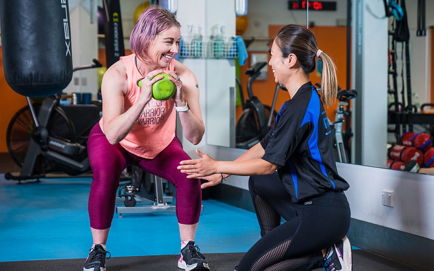 A female personal trainer assisting a woman in pink through a kettle bell workout at Christchurch Recreation and Sport Centre. 