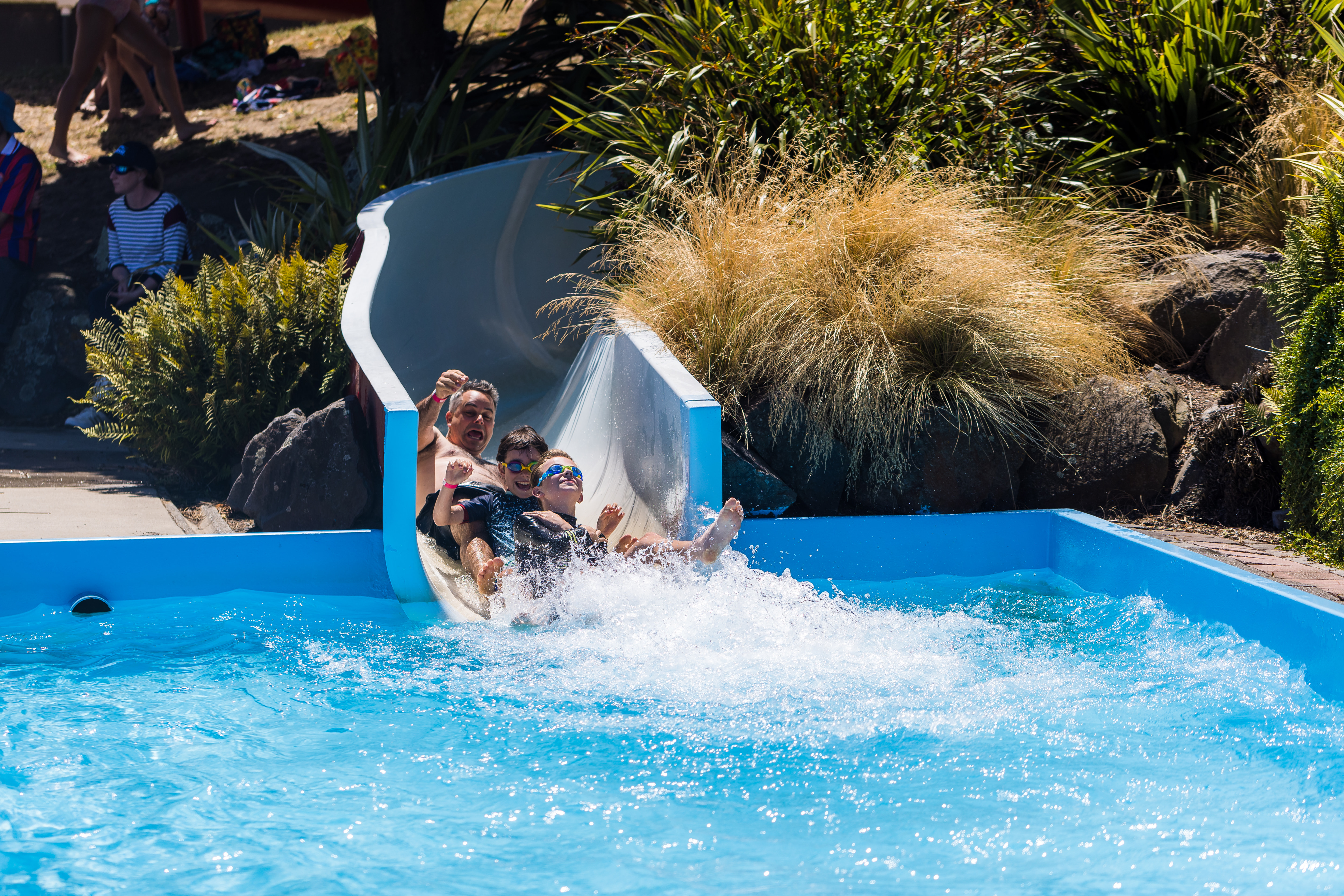 Two smiling boys and a man sliding down the Summer Pool hydroslide. 