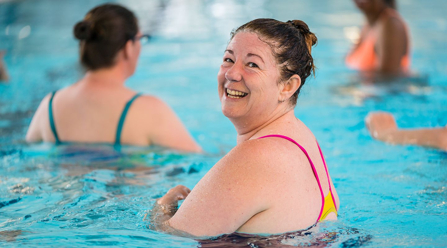 A smiling woman in pink swimmers participating in an Aqua Gentle class at Taiora QEII Recreation and Sport pool.