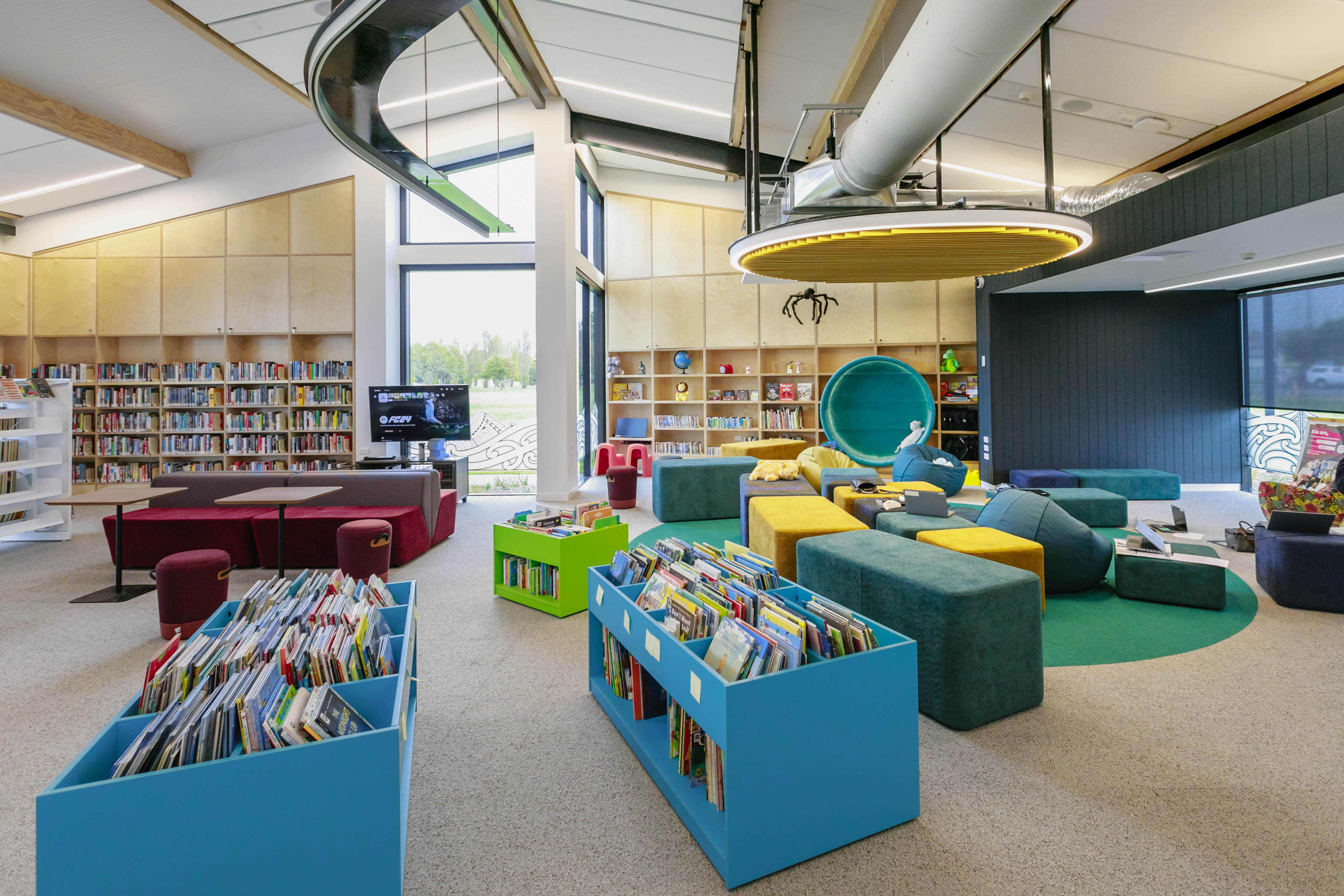 The Matatiki Hornby children's library area with bright blue bookcases, burgundy couches, and mixed green and yellow soft blocks for seating. 