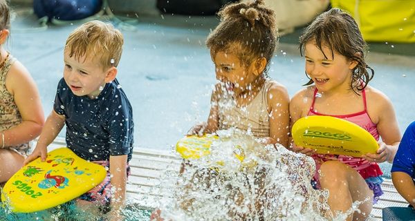 A group of smiling children holding flotation boards while attending a Dolphins class at Christchurch Recreation and Sport pool. 