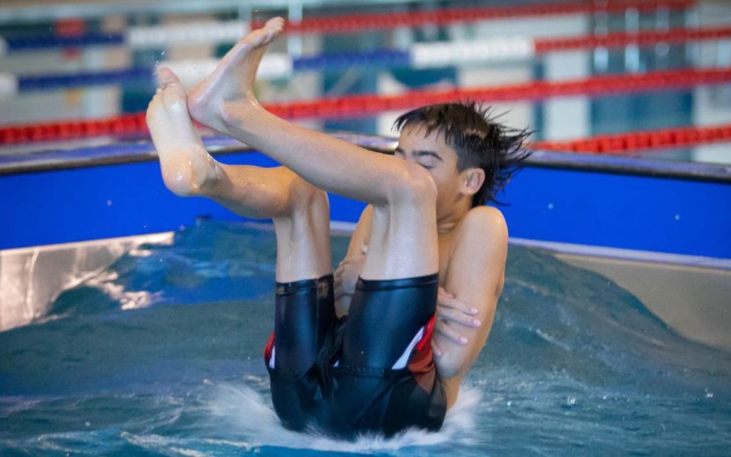 A teenage boy doing a manu off a diving board at Christchurch Recreation and Sport pool. 