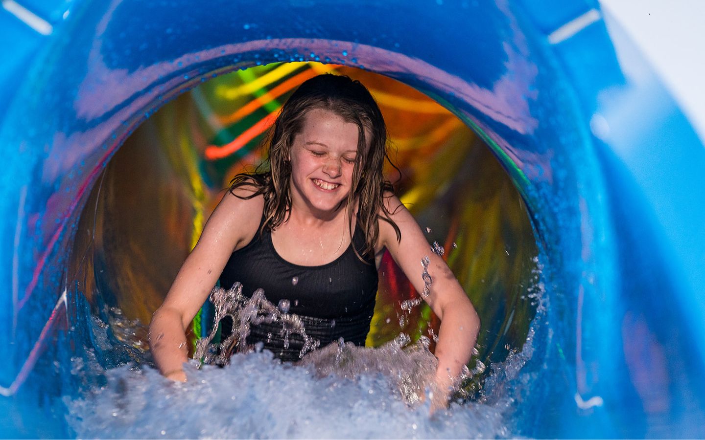 A smiling girl sliding down the blue hydroslide at Jellie Park outdoor pool. 