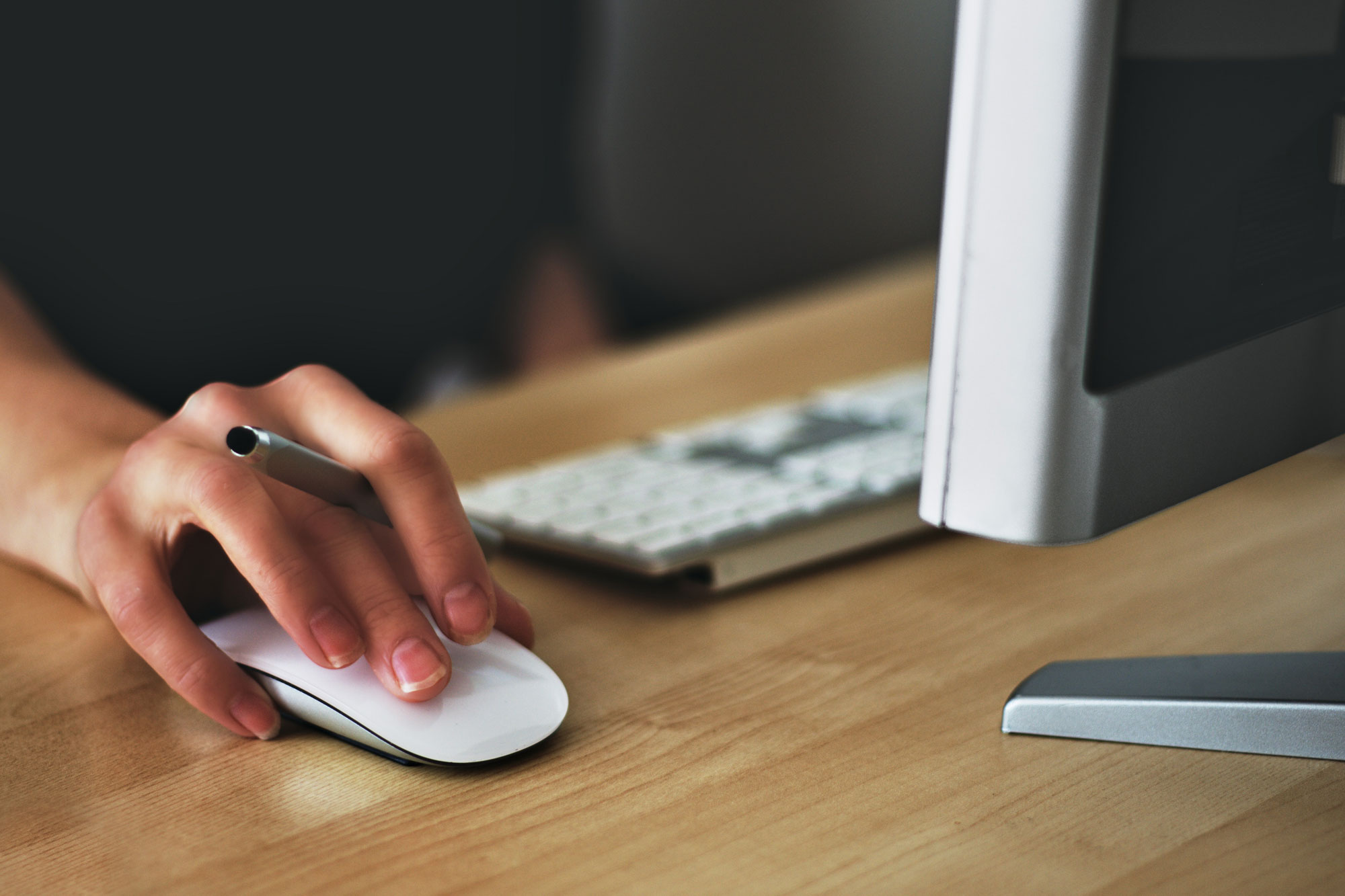 A person seated at a desk working on a computer using a white mouse. 