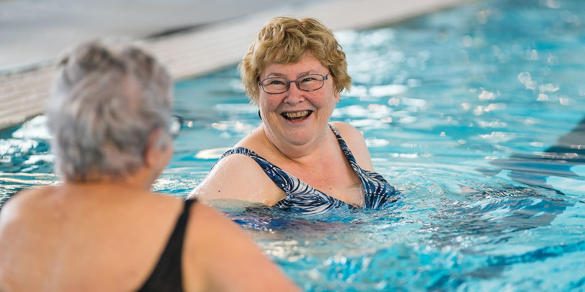 Two older women smiling in the pool while participating in an Aqua gentle class at Christchurch Recreation and Sport pool.