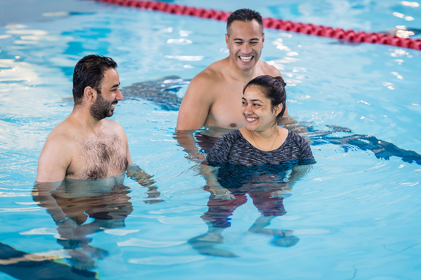Two men and a women standing in the pool smiling at one another at the Jellie Park Rec Centre. 