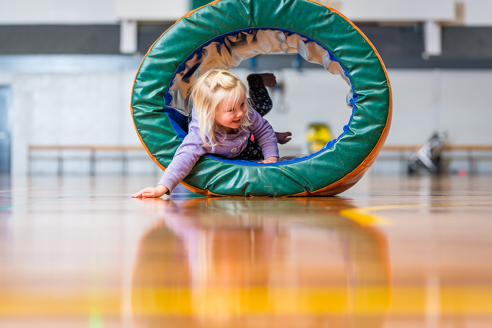 A smiling toddler hiding inside a foam ring during a Tumbletimes class at Christchurch Recreation and Sport Centre.