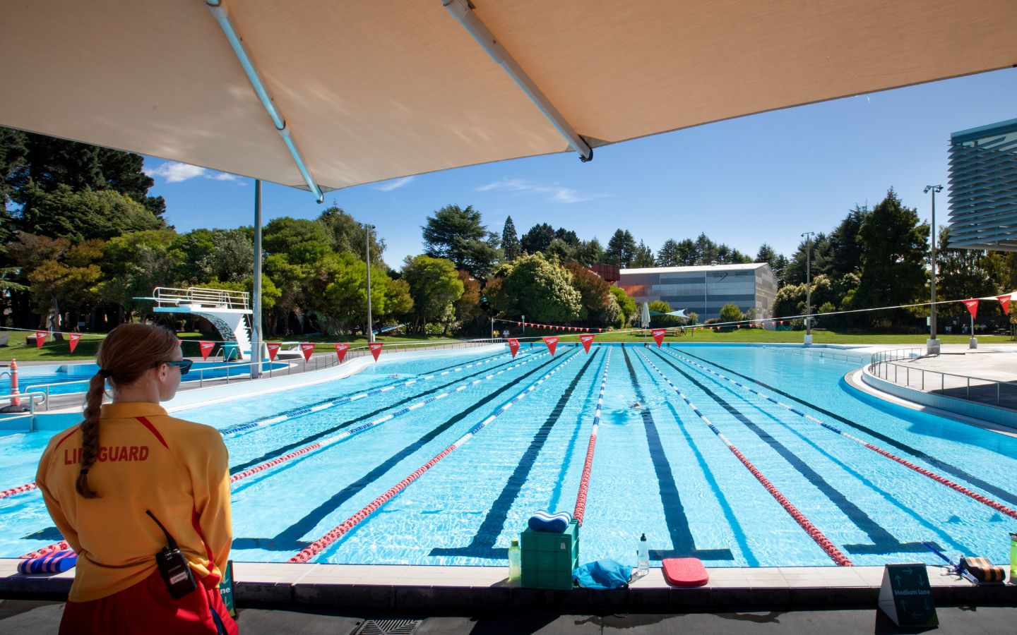 Female lifeguard standing under the shade behind the outdoor summer pool. 